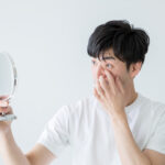 目やにが止まらない原因を特定し、結膜炎との見分け方や正しい対処法を決定するために、医師による診察や鏡を用いた症状の確認・指導を受けている男性の様子の写真